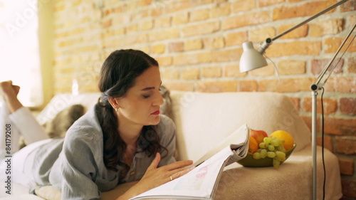 Woman reading magazine on the sofa and smiling to the camera
