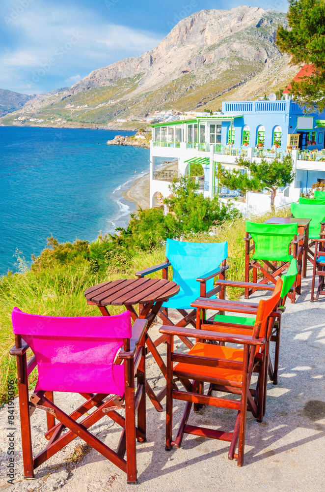 Fototapeta premium Colorful wooden chairs with view on sea, Greece