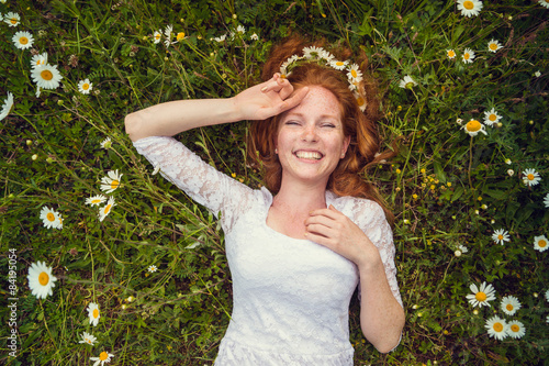 Beautiful young girl with curly red hair in camomile field