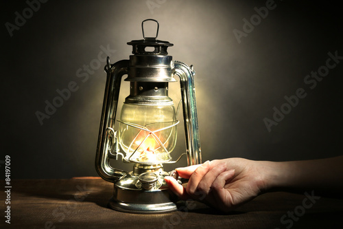Hand lights a kerosene lamp on dark grey background © Africa Studio