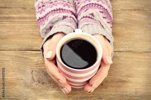 Female hands holding cup of coffee on wooden background