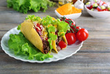 Tasty taco with vegetables on plate on table close up