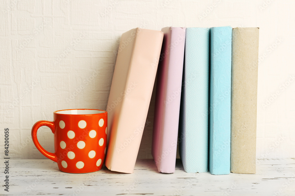 Fototapeta premium Books and cup on wooden shelf on wallpaper background