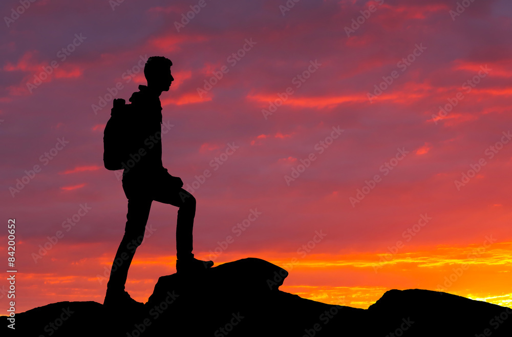Silhouette of a mountaineer standing on the top at sunset
