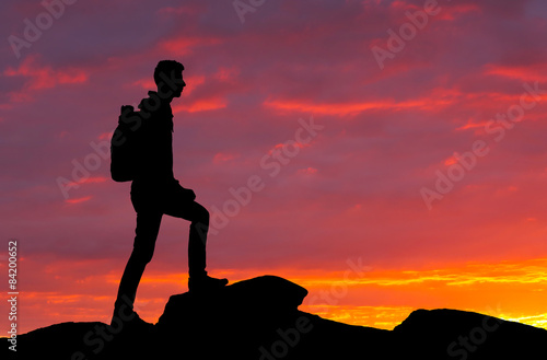 Silhouette of a mountaineer standing on the top at sunset