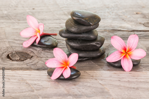 Plumeria flowers and black stones on weathered wooden background