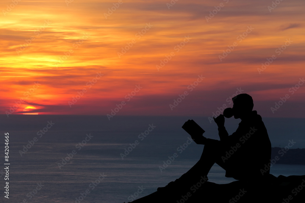 Silhouette of a man sitting on breakwater in evening near sea, r