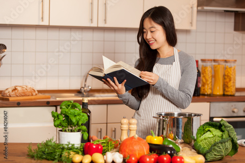 Asian smiling woman looking a cookbook