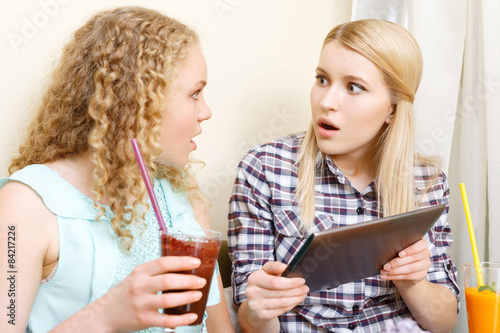 Two amazed girls with tablet in cafe
