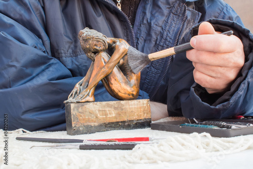 Hands of sculptor hold copper sculpture and clean it with brush photo