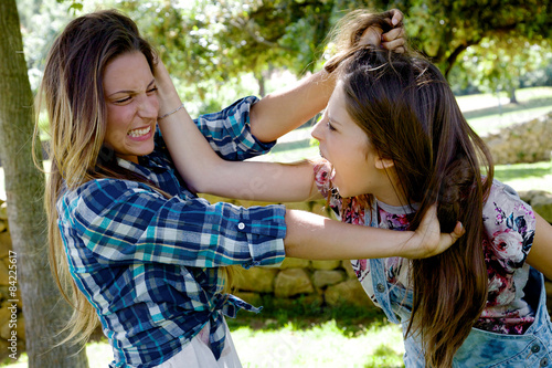 Two teenager friends fighting in park angry pulling long hair