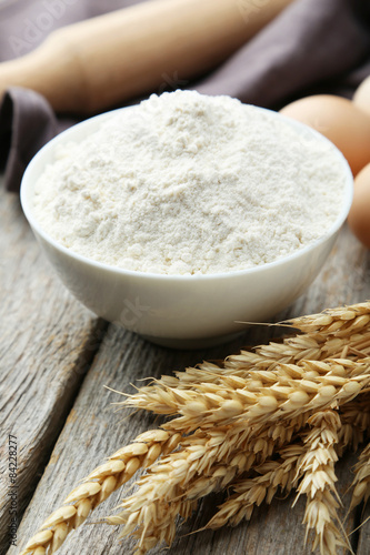 Bowl of wheat flour with spikelets on grey wooden background
