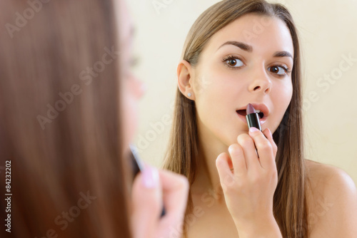 Girl applying lipstick at mirror. 