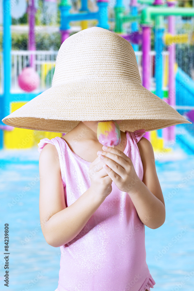Child with hat eating ice cream at pool