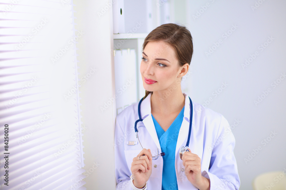 Woman doctor is standing near window with crossed arms,isolated Woman doctor is standing near window with crossed arms,isolated