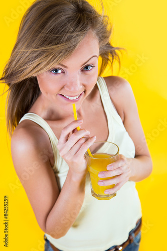 Teenager girl drinking orange juice on yellow background