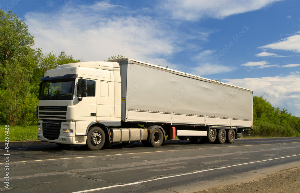 White truck on asphalt road under blue sky with clouds.