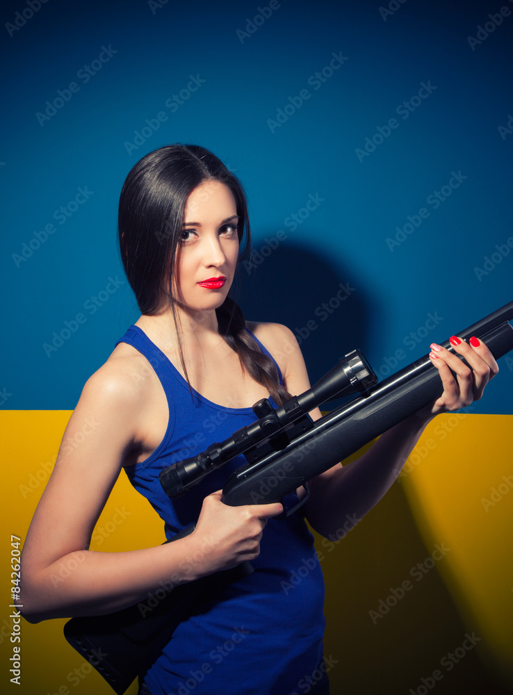 beautiful young woman posing with rifle against blue and yellow