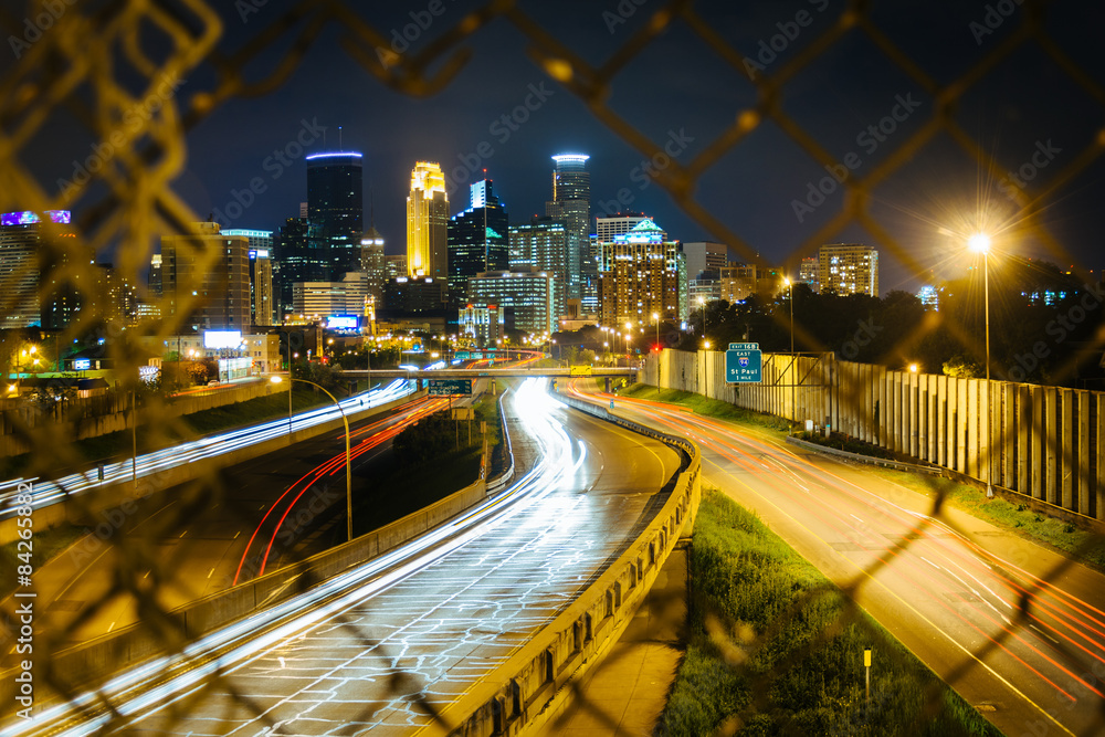 Chain link fence and view of I-35 and the skyline at night, seen