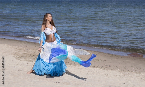 Belly dancer in blue costume on the beach with fans