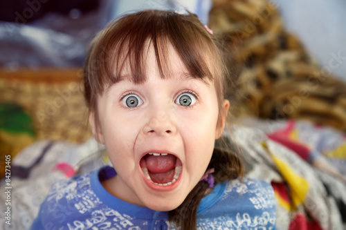 Shocked screaming little girl with opened mouth in her bedroom