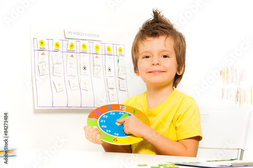 Smiling boy holding colorful carton clock sitting