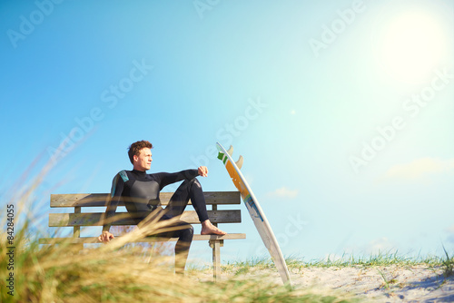 Surfer relaxing on a wooden bench on a dune