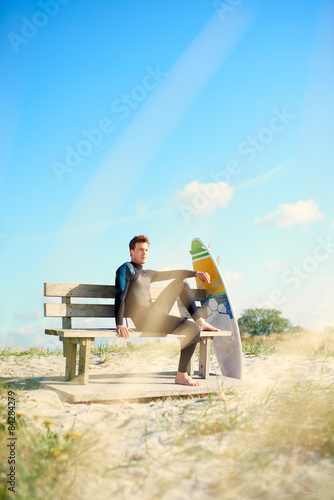 Surfer relaxing on a wooden bench with his board