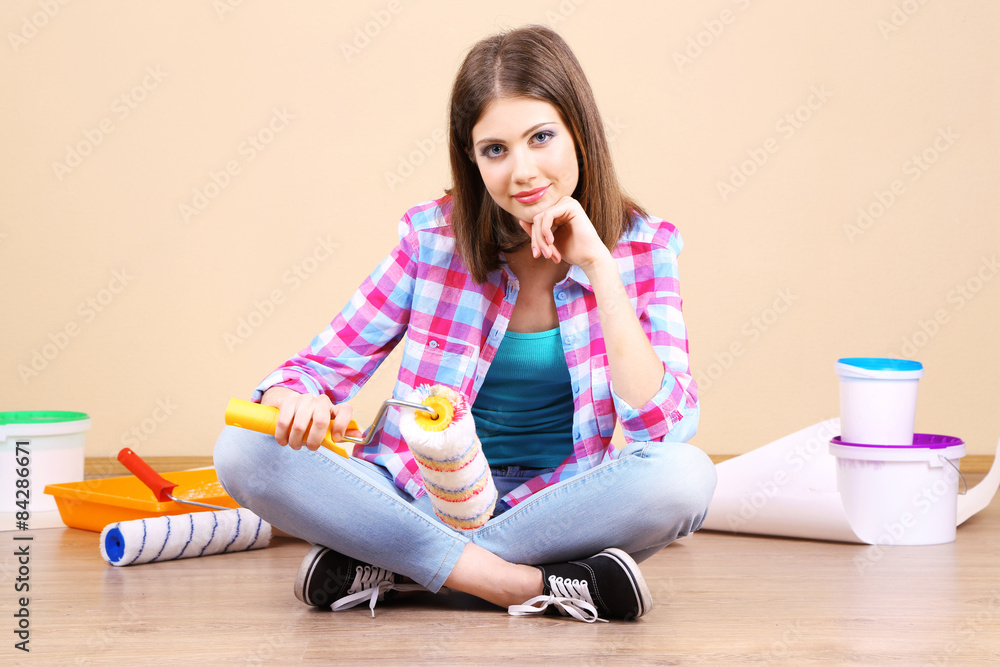 Beautiful girl sitting on floor with equipment for painting wall Beautiful girl sitting on floor with equipment for painting wall