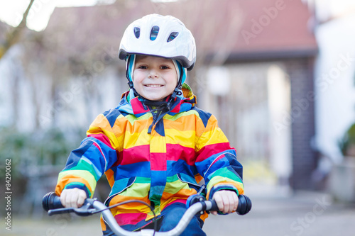 kid boy in safety helmet and colorful raincoat riding bike, outd © Irina Schmidt