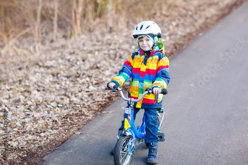 Fototapeta Naklejka Na Ścianę i Meble -  kid boy in safety helmet and colorful raincoat riding bike, outd