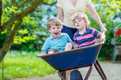 Two little boys having fun in a wheelbarrow pushing by mother photo