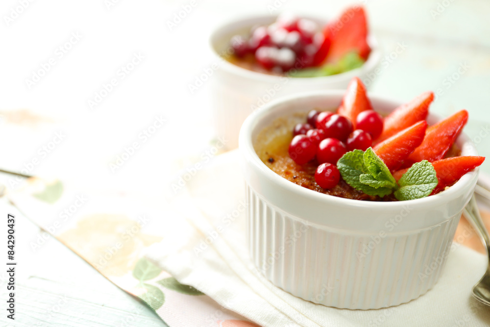 Creme brulee dessert with fresh strawberries and mint leaves, on color wooden background Creme brulee dessert with fresh strawberries and mint leaves, on color wooden background