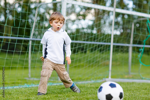 Two little sibling boys playing soccer and football on field