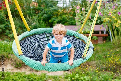 Adorable toddler boy having fun chain swing on outdoor playgroun photo