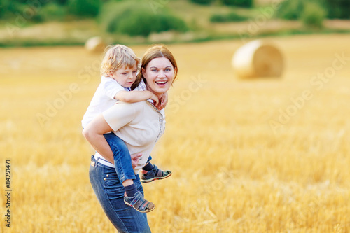 Young mother and her little son having fun on yellow hay field