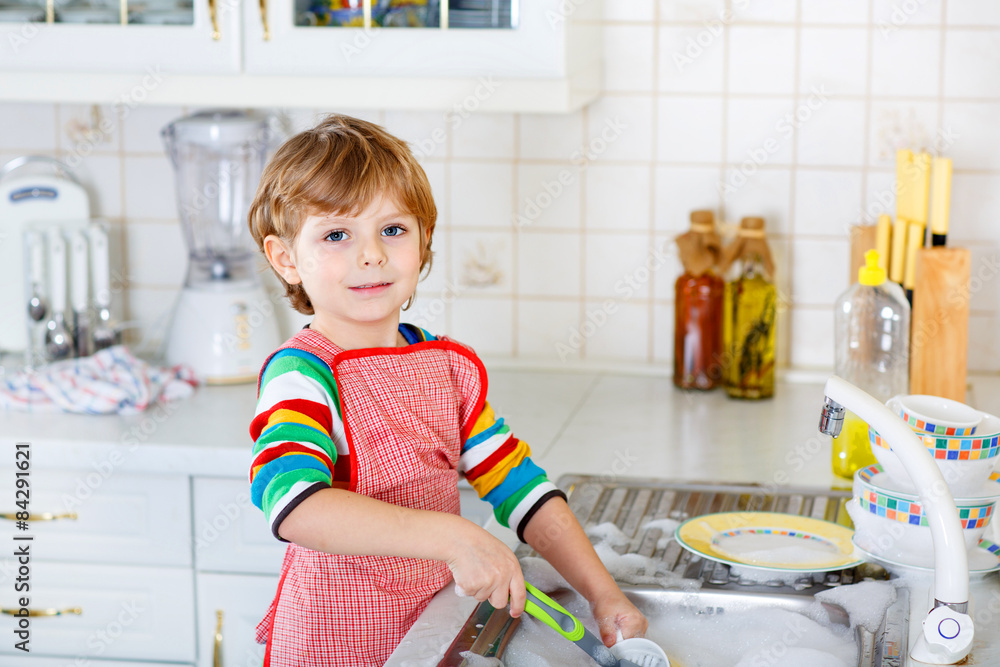 Funny kid boy helping and washing dishes at home - obrazy, fototapety, plakaty 