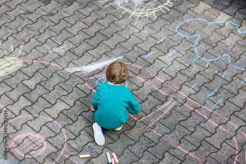 Little blond boy painting with colorful chalks outdoors