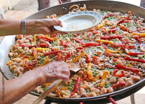 hand of the chef adds shrimp in rice paella with seafood