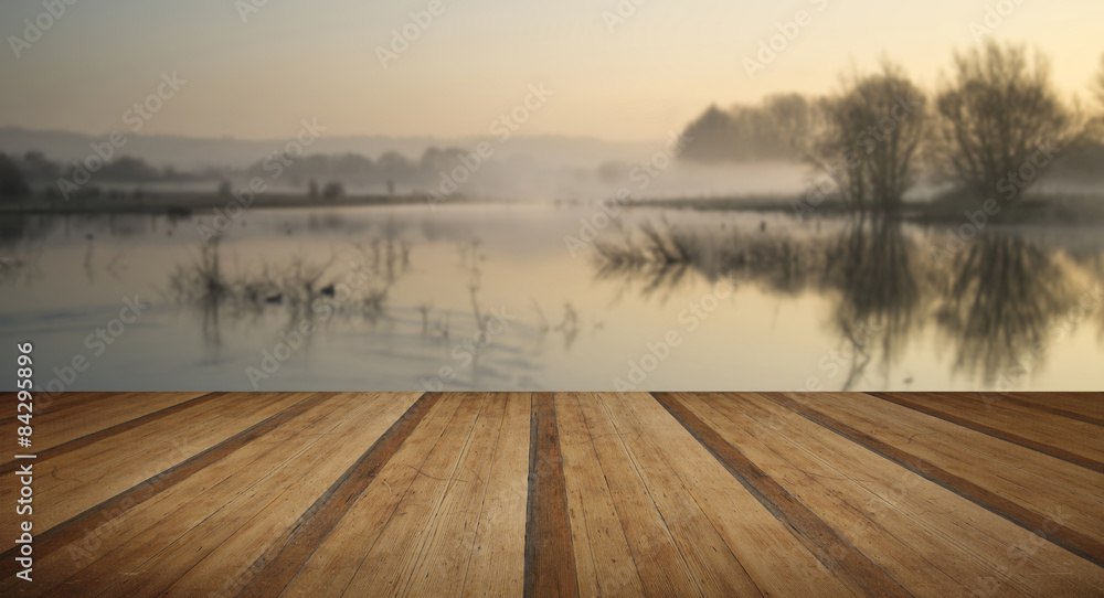 Fototapeta Landscape of lake in mist with sun glow at sunrise with wooden p