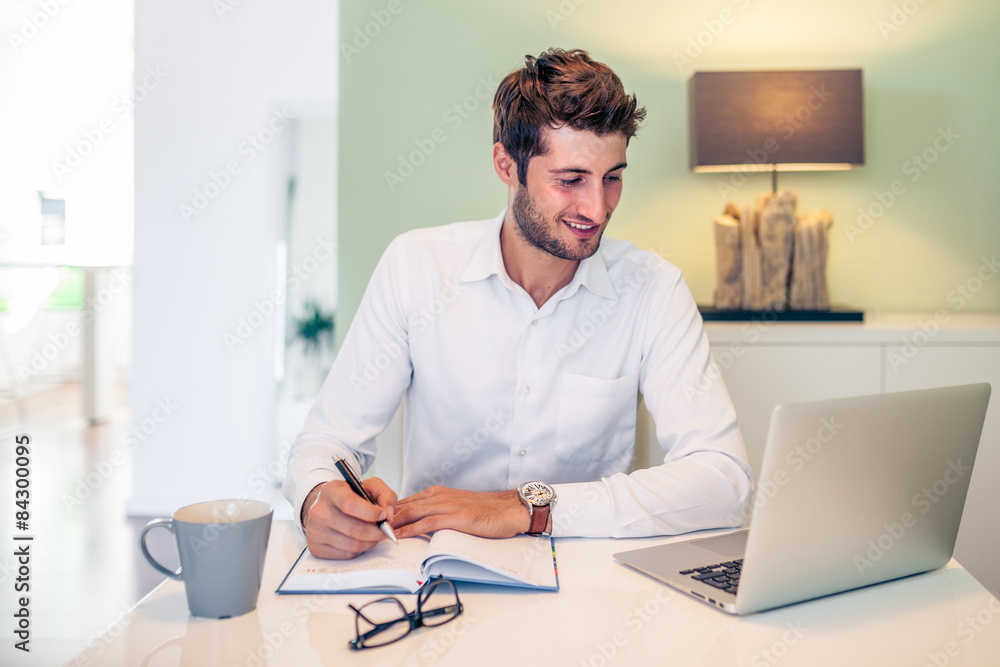 Handsome young smiling businessman working from home with a lapt Handsome young smiling businessman working from home with a lapt