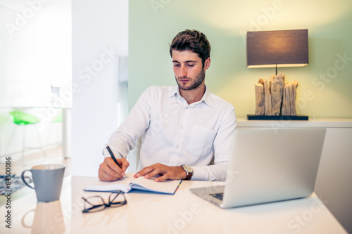 Handsome young smiling businessman working from home with a lapt