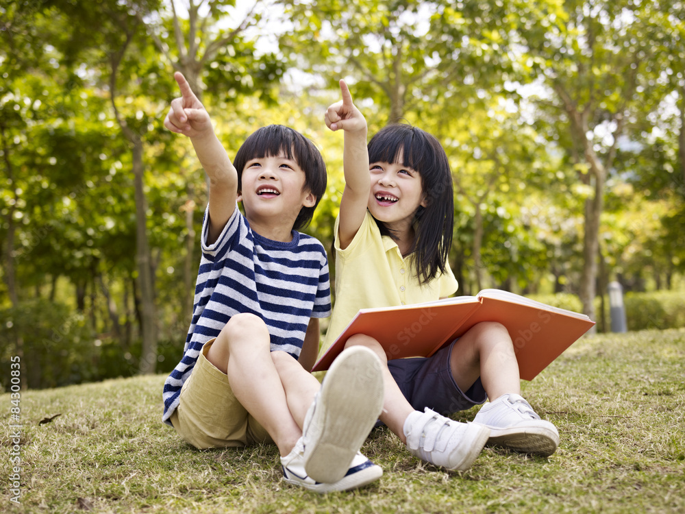 two beautiful asian children sitting on grass pointing to sky two beautiful asian children sitting on grass pointing to sky