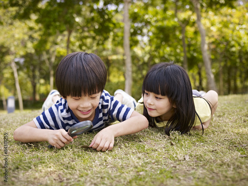Canvas Print asian children playing with magnifier outdoors