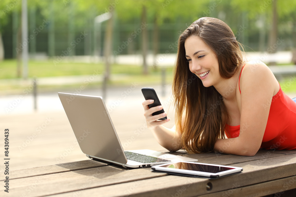 Girl using a laptop and smart phone in a park Girl using a laptop and smart phone in a park