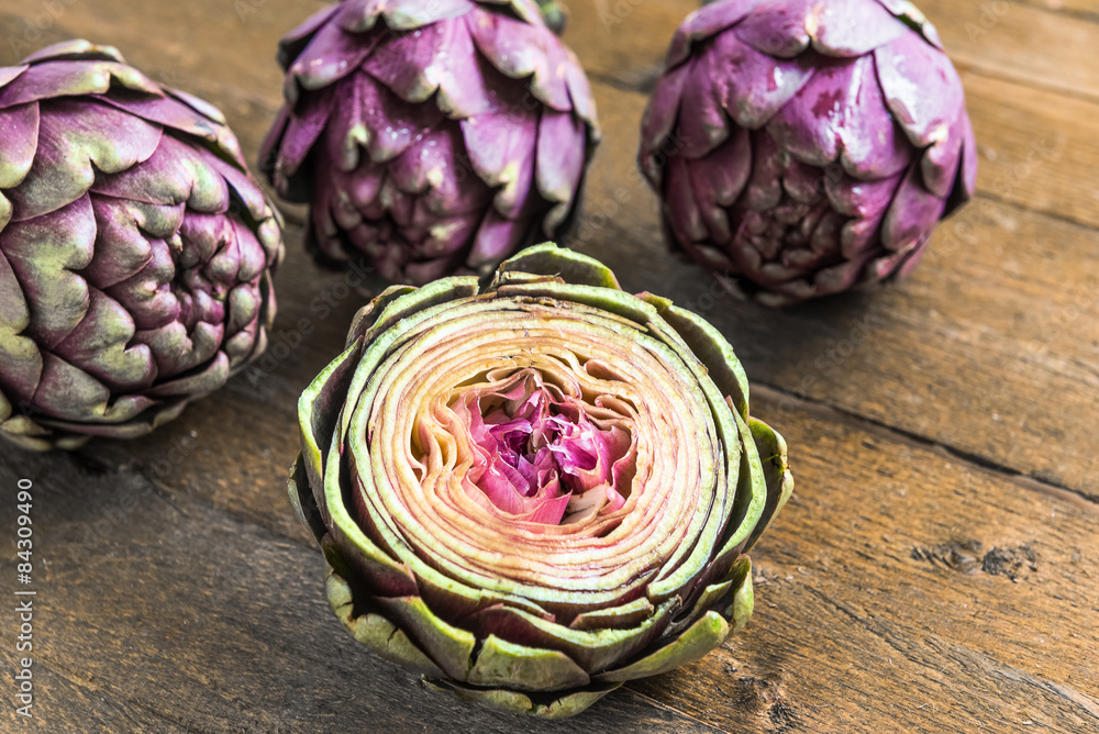 Obraz premium Three purple fresh artichoke and a half on wooden background