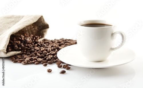 Cup of coffee with saucer with bag with coffee beans on white