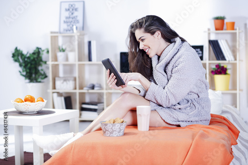 Woman in bed with coffee, tablet, computer, phone laughing