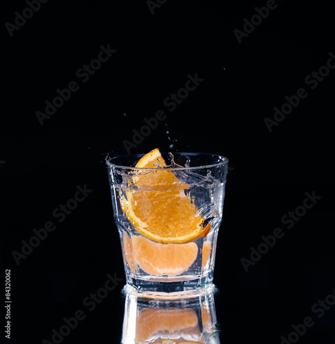 Slice of lemon splashing into a glass of water with a spray of water droplets 