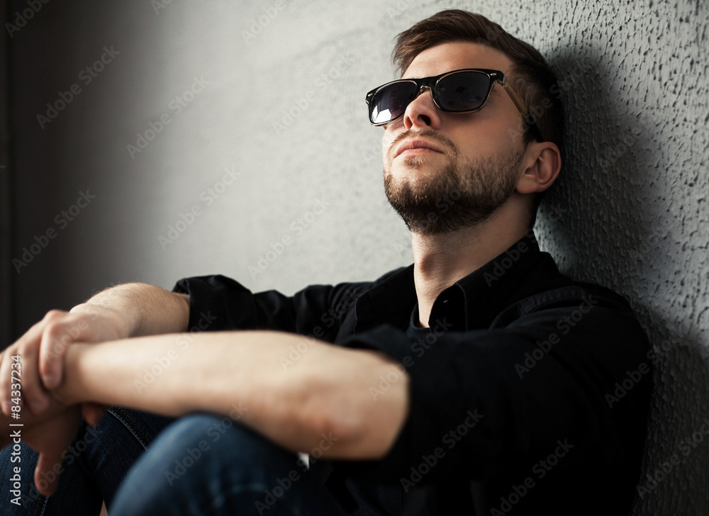 Obraz premium Young man in shirt siting with hands clasped against a wall